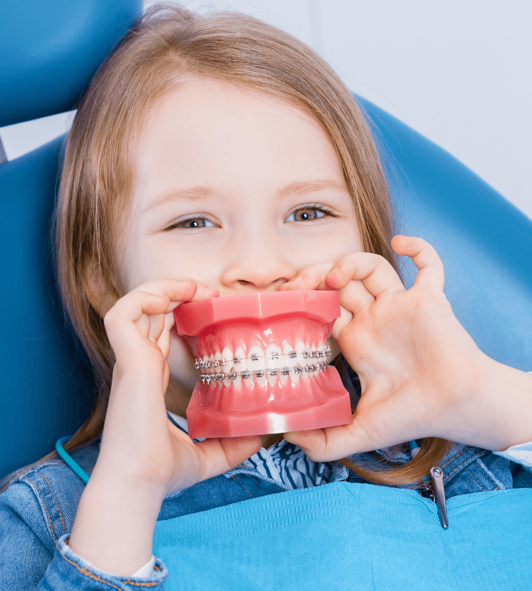 Niña sonriendo y jugando de forma divertida con un modelo dental educativo en el sillón del dentista, demostrando un entorno amigable y sin miedos en la consulta.