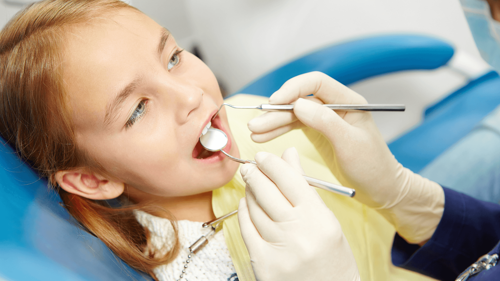 Niña pequeña tranquila y relajada mientras un dentista infantil examina su boca con un espejo dental durante su primera revisión en Mérida.